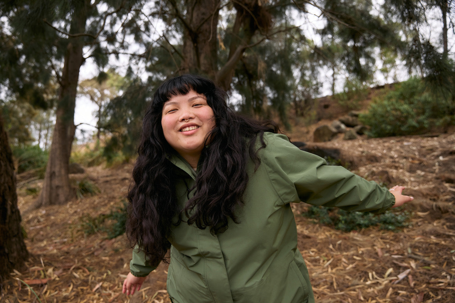 A model wearing the Refuge Jacket in Fern smiling happily in nature