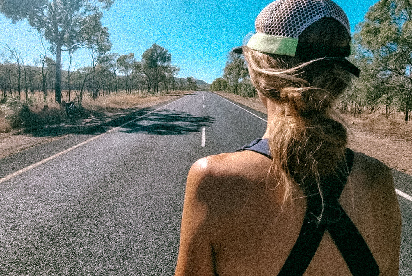 Woman in sports apparel staring at a wide open country road
